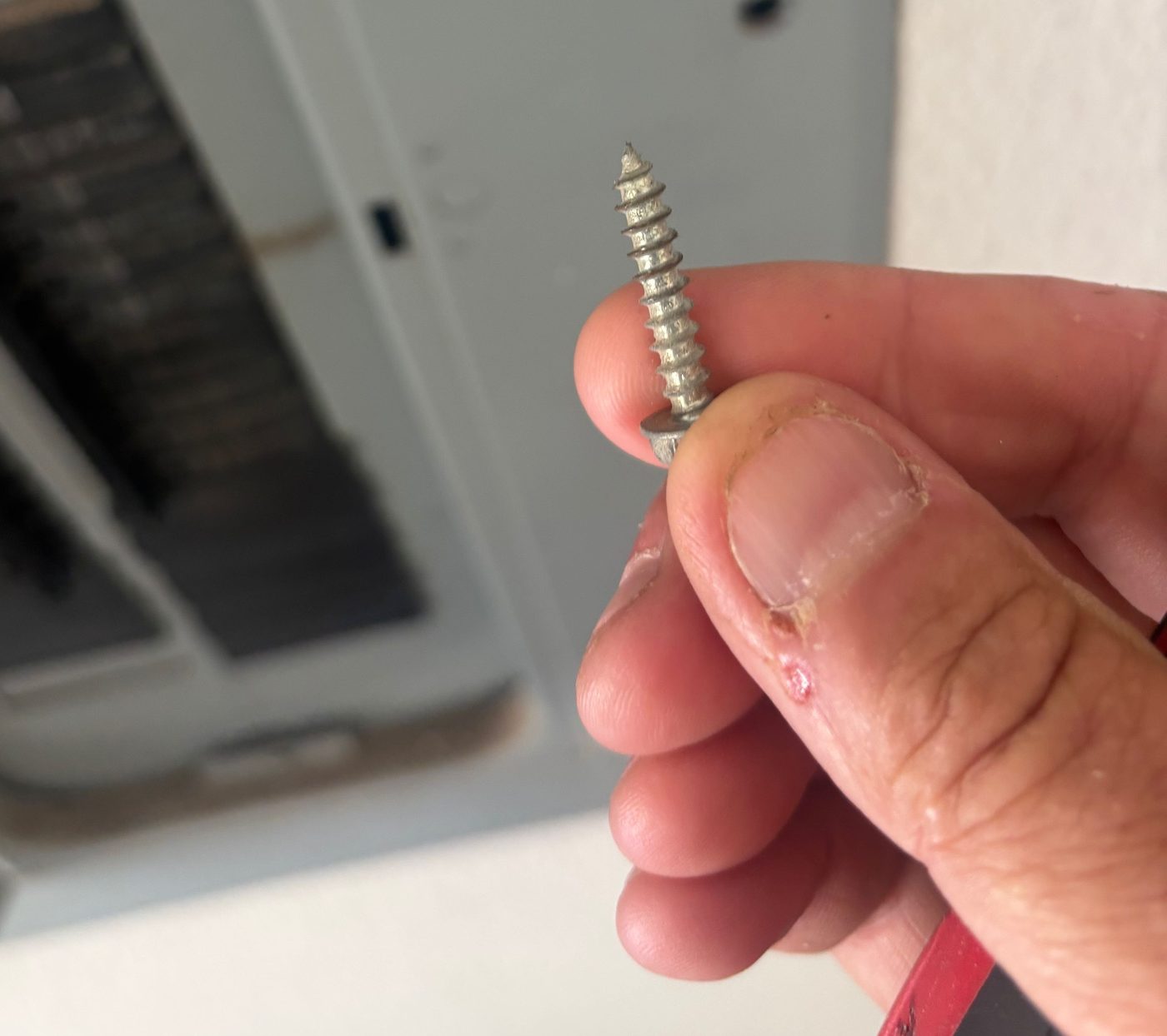 A pointed sharp-tipped screw held in front of an open electrical panel