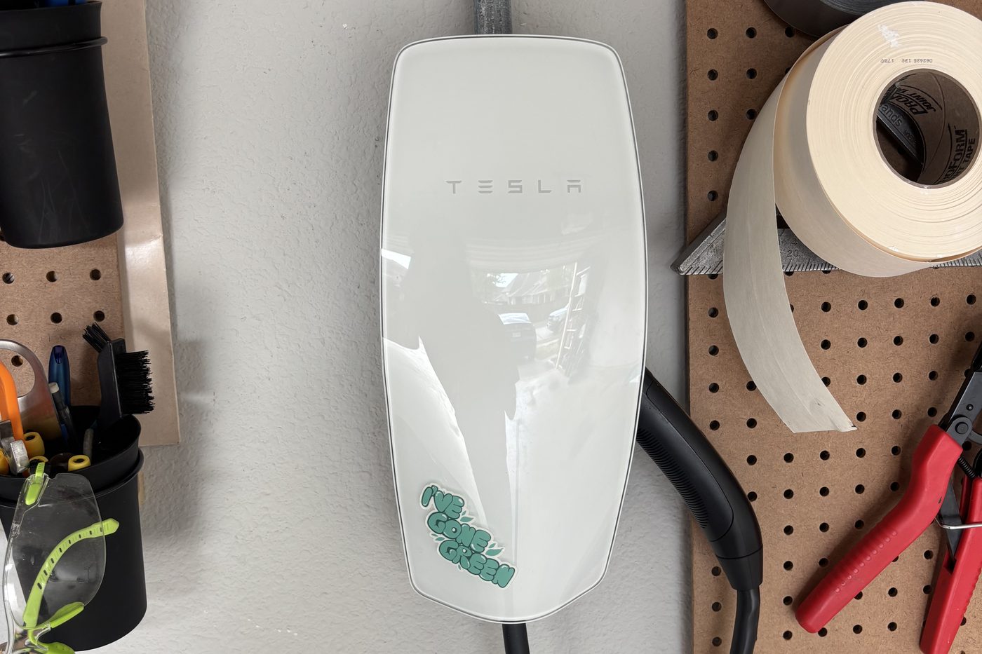 Tesla Wall Connector mounted on a garage wall, fed by conduit from above, with its charging cable hanging beside it